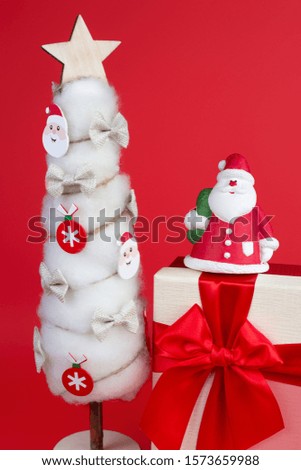 Gypsum colorful santa claus on the gift box and christmas tree with decorations over red background.