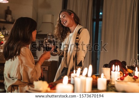 Photo of nice cheerful women drinking wine and laughing while having Christmas dinner in cozy kitchen