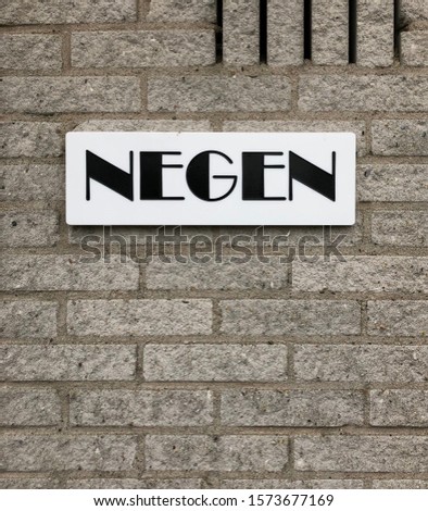 Written house number, negen means nine, on a grey brick wall, Almere, november 2019