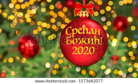 Text "Merry Christmas" written Cyrillic in Serbian. Blurred background of Christmas tree decorated with bright golden lights, toys, illumination. Bokeh. Happy New Year 2020. Greeting Postcard Serbia.