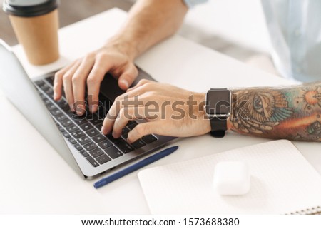 Cropped photo of a man with tattoo using laptop computer sit at the table in office