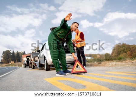 Repairer, transports a broken car on the road and placing a triangle
