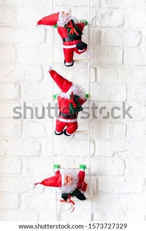 Climbing red santa claus on ladder agains white brick wall .