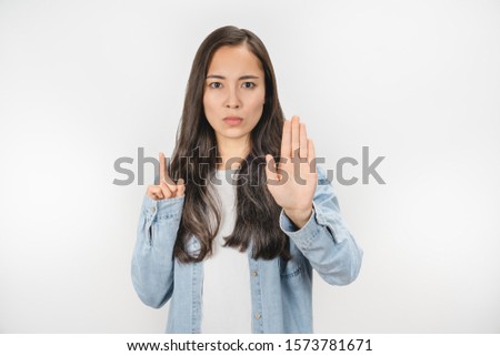 Portrait of serious young asian woman standing with hand showing stop gesture isolated over white background