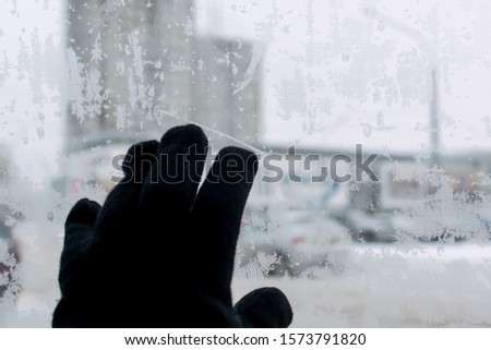 the hand of a man in a winter glove touches the icy glass of the car, on which snow patterns, snowflakes, on the background of the cityscape. Cold in the car