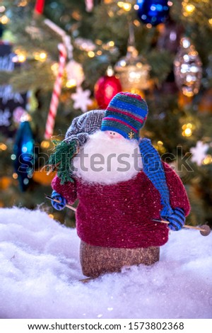 An old bearded santa doll skis into christmas with a bag over his shoulder holding toys ad a tiny tree