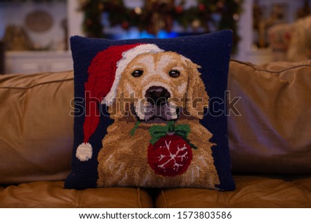 A cute pillow of a dog holding a Christmas ornament while wearing a Santa hat. 