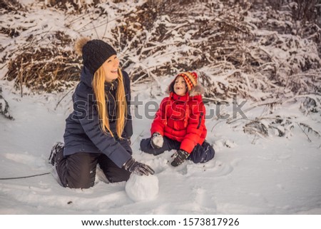 Happy family in warm clothing. Smiling mother and son making a snowman outdoor. The concept of winter activities