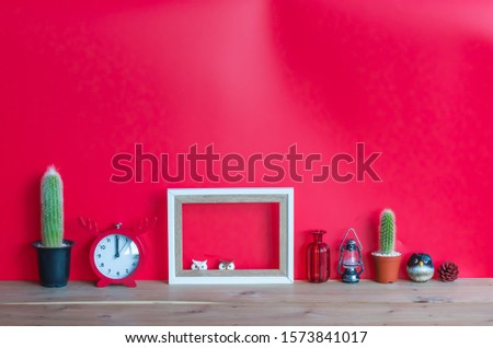 Cactus,blank  wooden  picture  frame,simulated  owl,  clock,  bottle,replica  lamp  and  pine  cone  on  wood  table  with  red  background,mockup