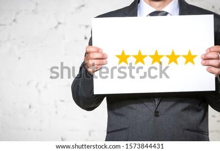 Man in suit holding white placard with five yellow stars rating against brickwall