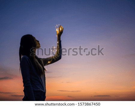 Happy young womanholding fairy lights in sunset, outdoor