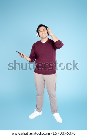 Happy Asian man wearing sweater  using headphone and smartphone on blue background.