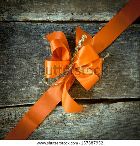 Ornamental diagonal orange ribbon and decorative bow on rustic dark textured wood with copyspace for your greeting or Christmas wishes