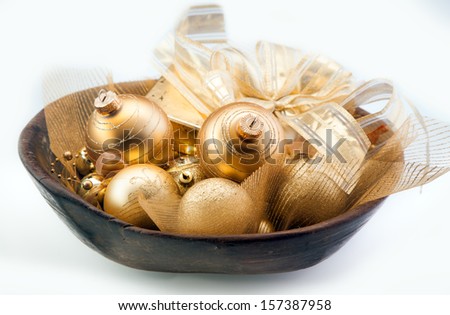 Colourful shiny collection of golden Christmas baubles, bows and ribbons in a wooden bowl over a white background