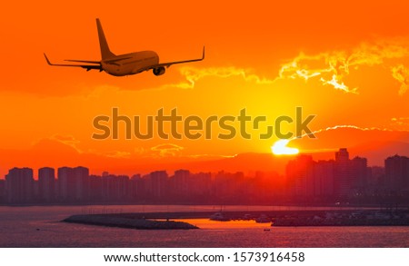 Commercial airplane flying above city in sunset 