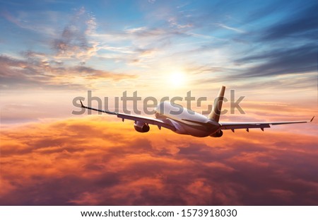 Passengers commercial airplane flying above clouds in sunset light. Concept of fast travel, holidays and business. Royalty-Free Stock Photo #1573918030