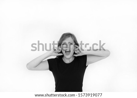 Black and white emotional portrait of an active and angry beautiful teenager girl screaming in pain covering her ears with her fingers during an ensemble rehearsal in the studio. Lifestyle. Isolated