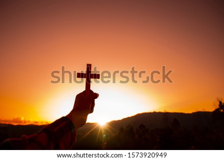 Human hand holding cross with a sunset sky background. Christian silhouette concept.
