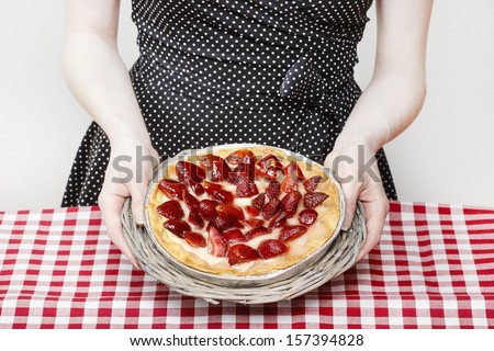 Woman holding round strawberry cake over kitchen table