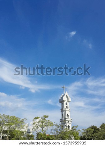 The clear sky saw the cross. At the top of a tall tower with trees and roofs.