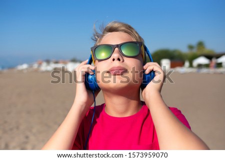 Closeup view of handsome white young kid listening to music outdoor standing on sunny summer beach. Horizontal color photography.