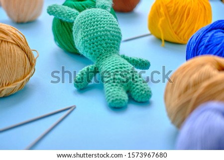 Bright color yarn clews with pastel green stuffed bunny on the blue background. Concept of amigurumi toy making, handcrafting, knitting, hobbie.