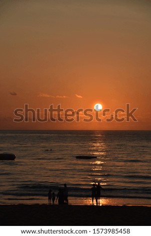 Sunrise over the ocean with human silhouettes. Sunlight reflects on sea water over some waves.