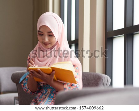 Muslim concept. Young muslim woman writing notebook paper, relaxing and enjoying her book. 