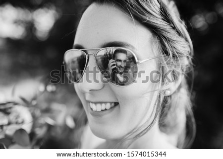 Wedding closeup portrait of a smiling bride with reflection of groom in sunglasses. An interesting idea in photography, concept. Black and white photography.