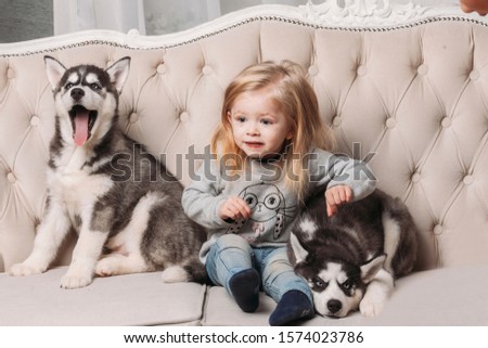 blonde girl with Husky puppies sitting on a beige couch