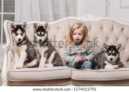 blonde girl with Husky puppies sitting on a beige couch