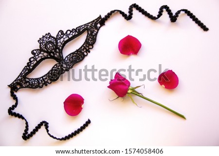 Black lacy carnival mask for women, red rose with petals on a white background. Flat lay. Copy space.