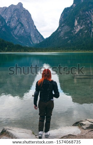 Red hair girl in body protection jacket turtle armor, walk adove the Alps mountain and lake. Vertical photo. Toblacher See, (Italian: Lago di Dobbiaco) a lake in South Tyrol, Italy.
