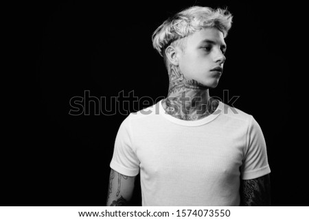 Studio shot of young handsome rebellious man with blond hair against black background in black and white
