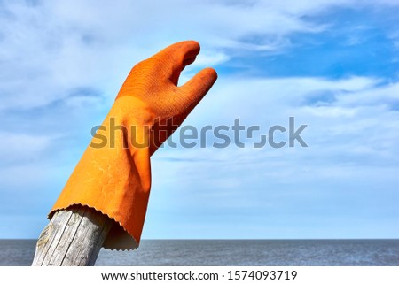 Rubber glove on wooden pole by the sea under a blue sky with clouds and copy space. Zero waste, plastic free, stop pollution, ecological concept.    
