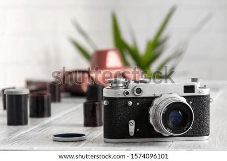Old camera, bag and films on a gray wooden table. A vintage camera stands on a table with photographic films.