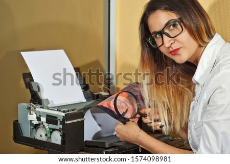 The girl in a white shirt prints a photo. Woman looking through photo with magnifier. The glasses assistant checks the printed image. Sunset in the photo.
