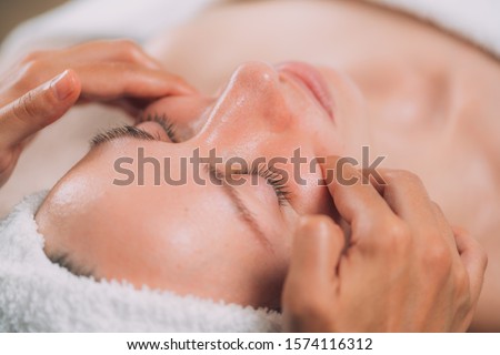 Facial massage beauty treatment. Close-up of a young woman’s face lying on back, getting face lifting massage, pinch and roll technique.  Royalty-Free Stock Photo #1574116312