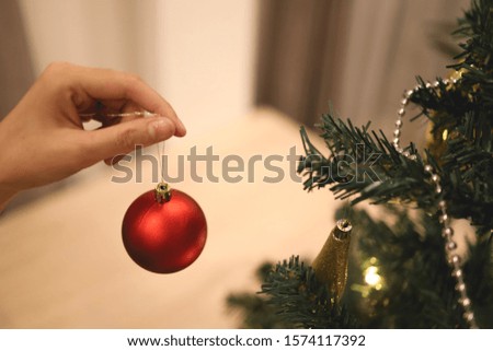 Close up pictures, woman hand decorating the Christmas tree with red balls