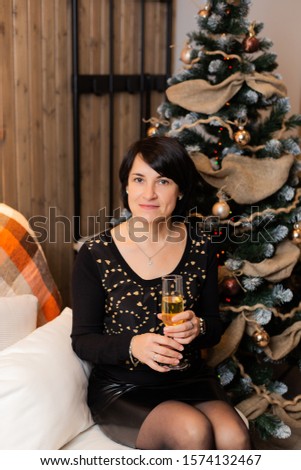 Beautiful woman 50 years old at the Christmas tree with a glass of champagne in the New Year. Woman portrait.