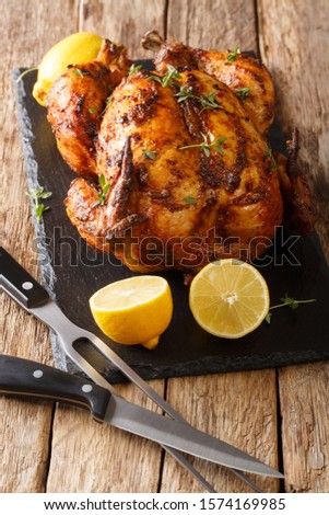 Homemade chicken rotisserie with thyme, lemon closeup on a slate board on the table. vertical
