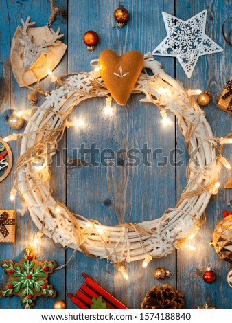 New year decorations around Christmas wreath burning lights garlands on blue wooden background. View from above. Flat lay. copy space
