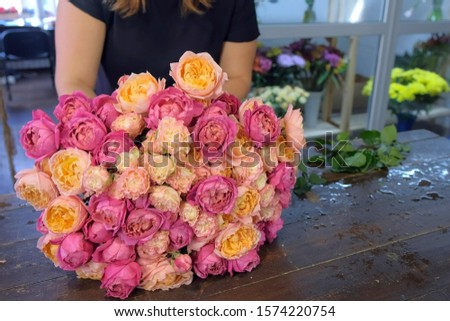 Florist woman making bouquet of pink and orange peonies in flower shop, closeup hands. Floral business concept. She creates professional bunch composition in floristic studio store at table.