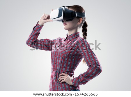 Young woman in checked shirt wearing virtual helmet against gray background