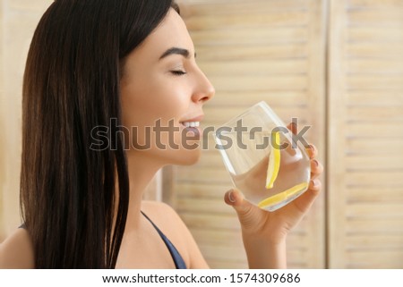 Beautiful young woman drinking fresh lemon water indoors