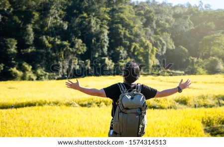 Rear view of traveller asian man with photograph style backpack. Open arm standing hug a nature at outdoor field.