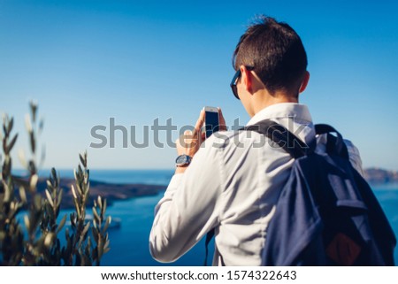 Santorini traveler taking photo of Caldera from Fira or Thera, Greece on phone. Tourist admiring Aegean sea landscape. Tourism, traveling, vacation concept.