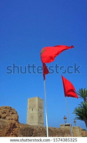    A Moroccan two flags fluttering near a mosque silo                             Royalty-Free Stock Photo #1574385325