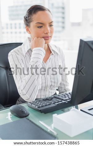 Thoughtful attractive businesswoman looking at computer screen in her office
