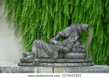 Hindu god Ganesha in lying position on a statue in front of a green and stone background